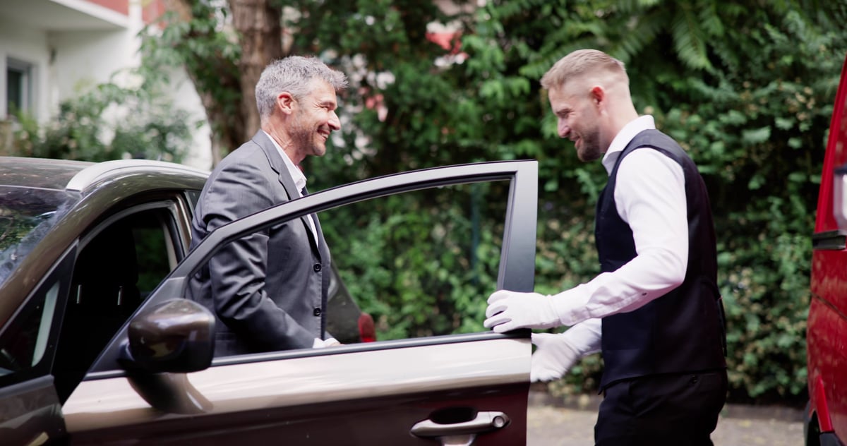 Man Giving Car Key To Male Valet Near Valet Parking Sign