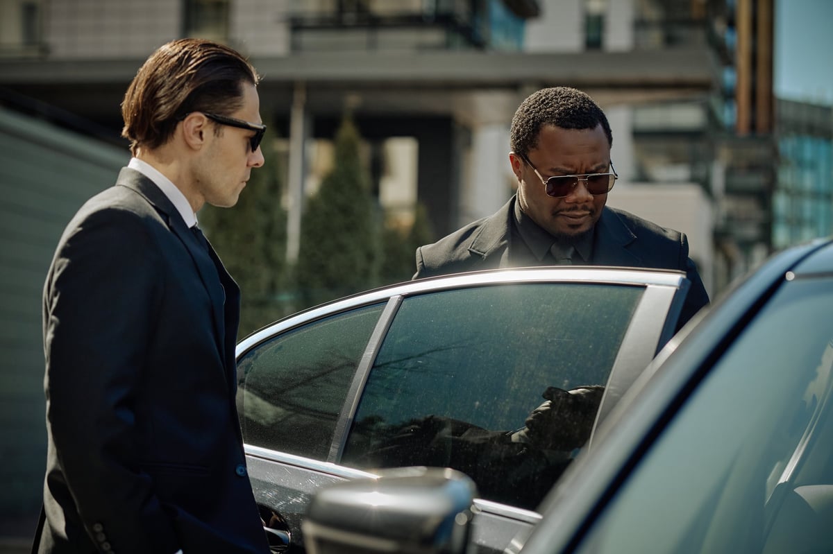 Professional chauffeurs in suits opening car door for executive transport service